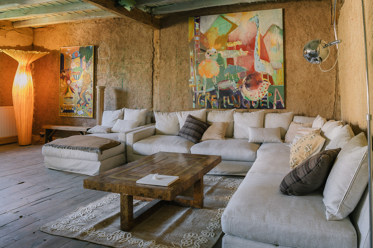 Sala de estar rústica con muebles de madera, sofás cómodos y arte colorido en las paredes. Ambiente cálido y ecléctico