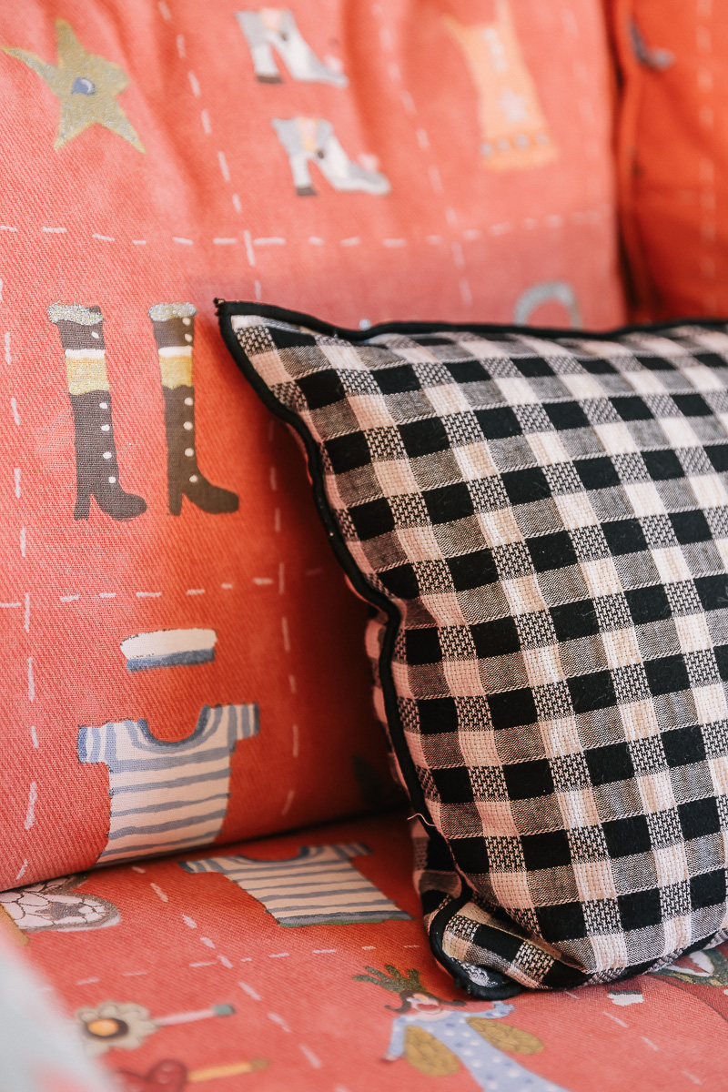 Deatlle tapiceria roja sofa y cojin cuadros vichy blanco y negros. Sala de estar rústica con muebles de madera, sofás cómodos y arte colorido en las paredes. Ambiente cálido y ecléctico.