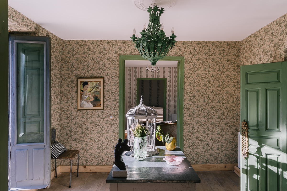Dormitorio de estilo rústico con muebles de madera, papel pintado de flores. Decoración en tonos verdes, lámpara vintage. Ambiente cálido y ecléctico.