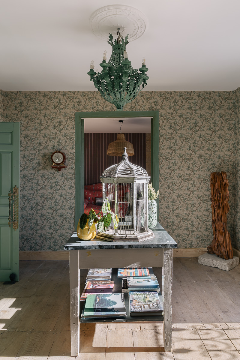 Dormitorio de estilo rústico con muebles de madera, papel pintado de flores. Decoración en tonos verdes, lámpara vintage. Ambiente cálido y ecléctico.