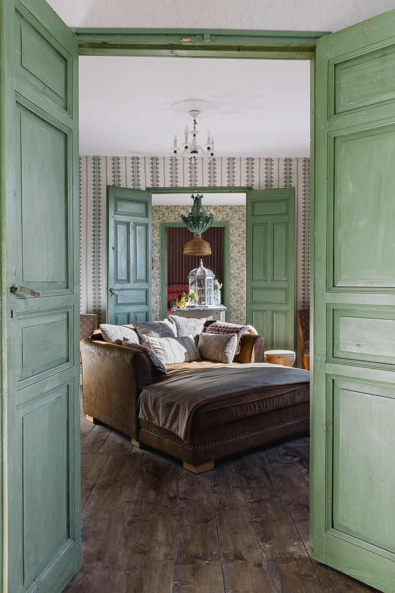 Dormitorio de estilo rústico con muebles de madera, papel pintado de flores. Decoración en tonos verdes, lámpara vintage. Ambiente cálido y ecléctico.