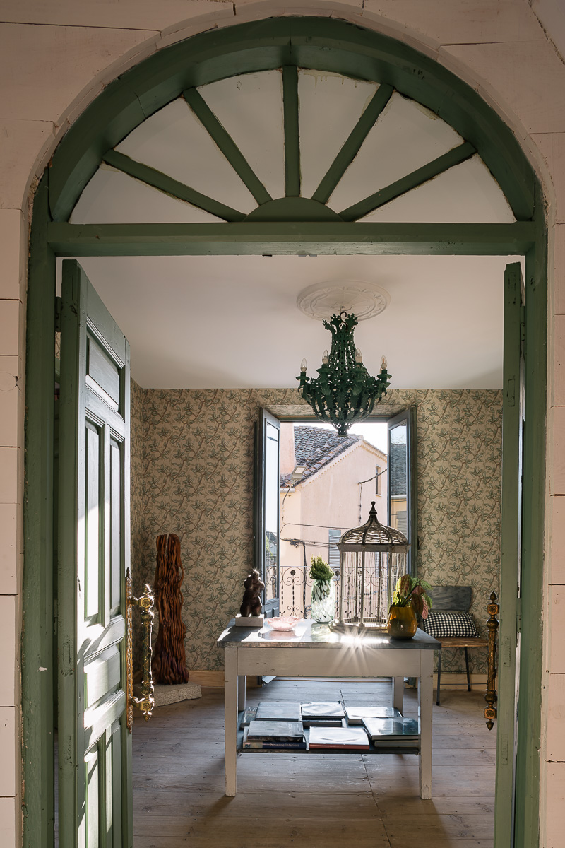 Dormitorio de estilo rústico con muebles de madera, papel pintado de flores. Decoración en tonos verdes, lámpara vintage. Ambiente cálido y ecléctico.