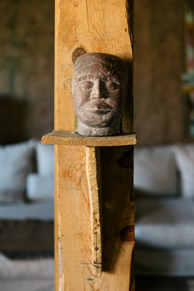 Detalle escultura casa rural. Salón rústico con muebles de madera, sofás cómodos y arte colorido en las paredes. Ambiente cálido y ecléctico