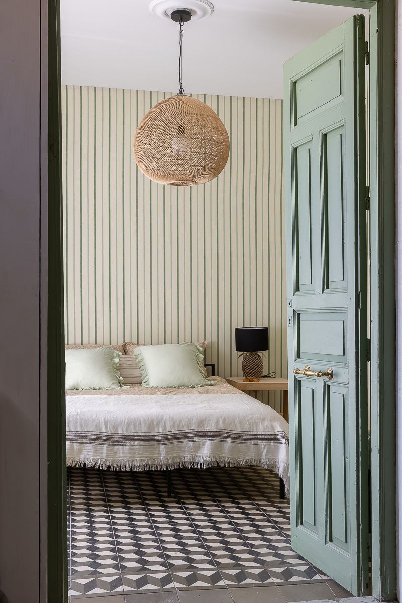 Dormitorio de estilo rústico con muebles de madera, papel pintado de flores. Decoración en tonos verdes, lámpara vintage. Ambiente cálido y ecléctico.